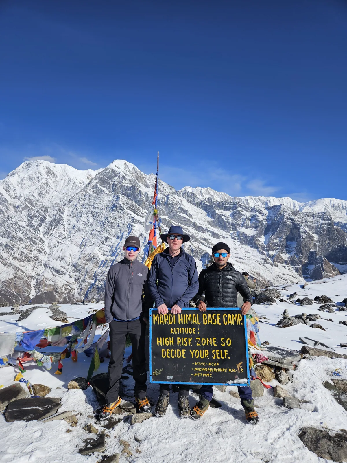 Trekkers at the Mardi Himal viewpoint sign surrounded by snowy Himalayan peaks